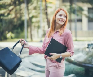 woman in pink suit holding a bag and smiling