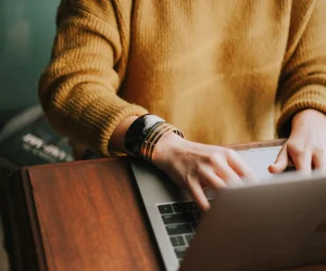 woman in brown sweater typing on laptop