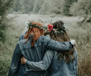women in denim jackets with flower wreaths in their hair holding each other behind their backs