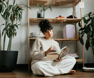 Woman in white sitting on wooden floor reading a book